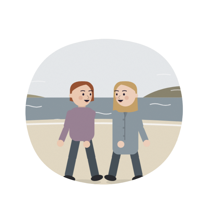 A woman walks along a windy beach with a friend, both laughing.