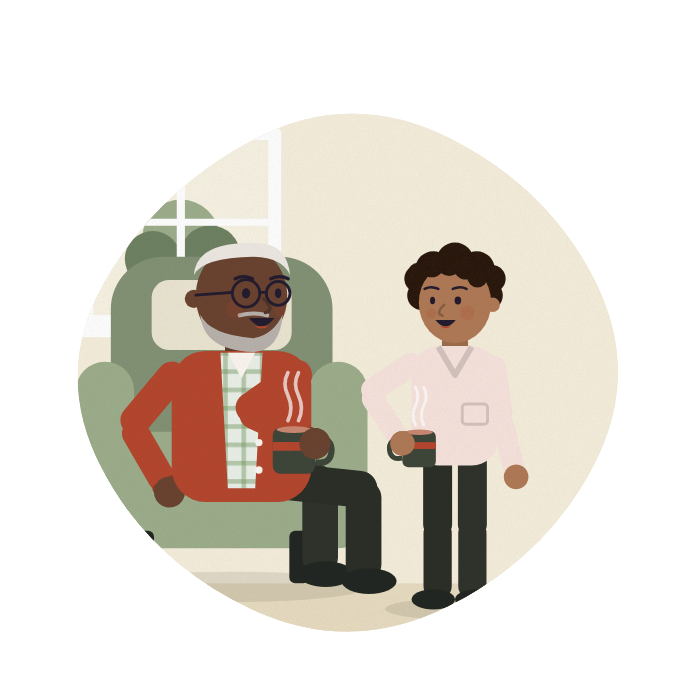 A carer and an older man share a laugh in his living room.