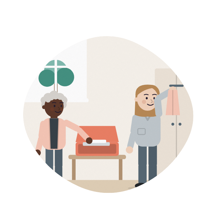 An older woman unpacks a small case in a bright room, a care worker hanging up her cardigan.